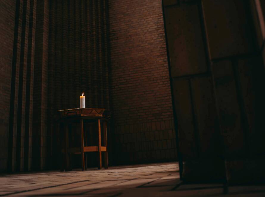 Lit candle on wooden table in brick room.