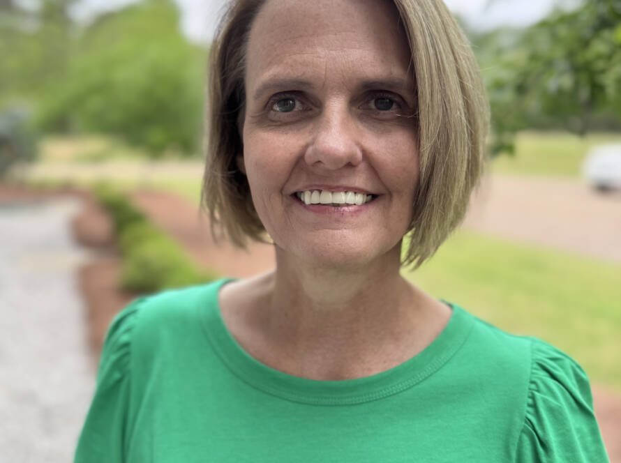 A woman in green shirt standing next to trees.