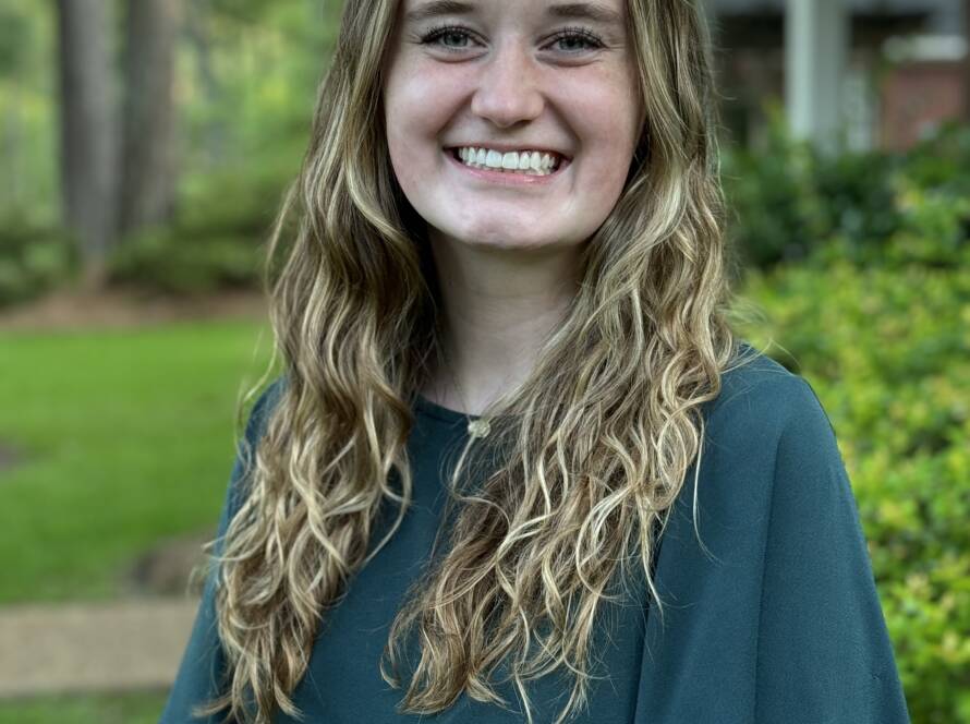 A woman smiling for the camera in front of some bushes.