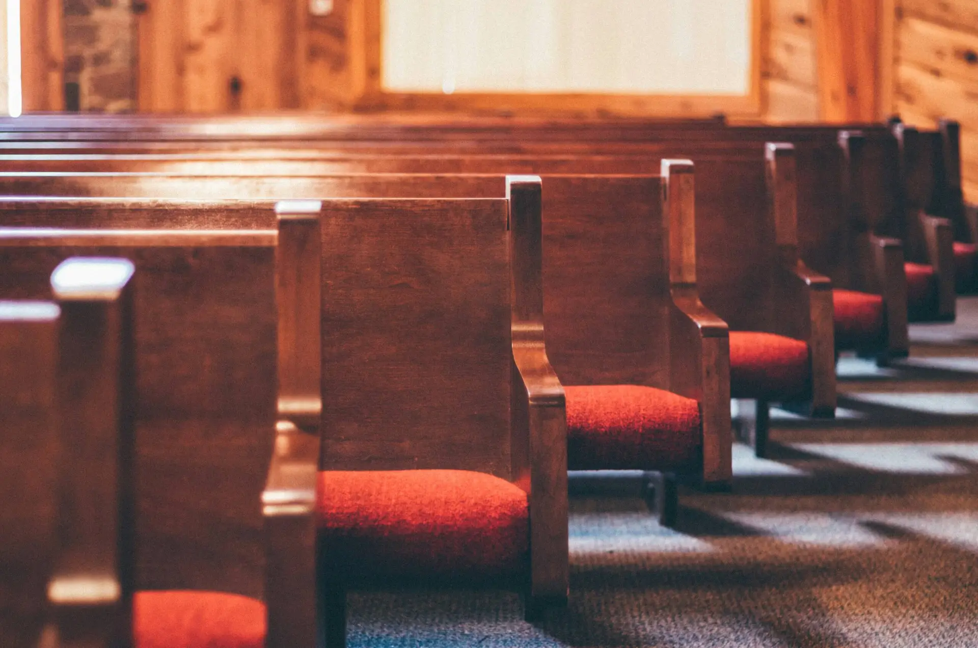 A row of wooden church pews with red seats.