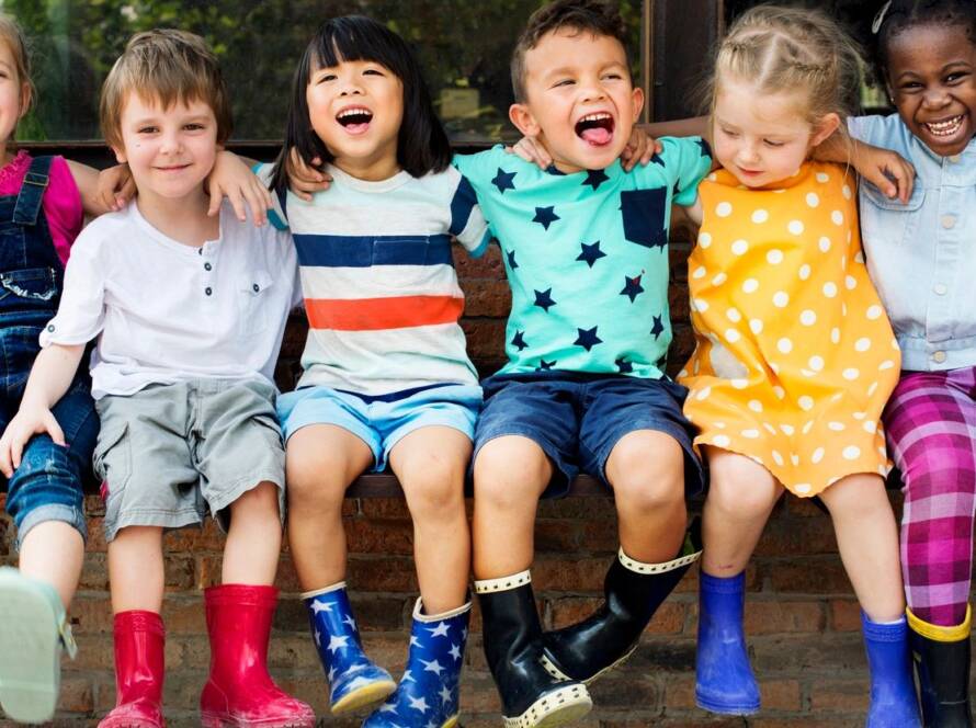 Children sitting, laughing, and wearing colorful boots.