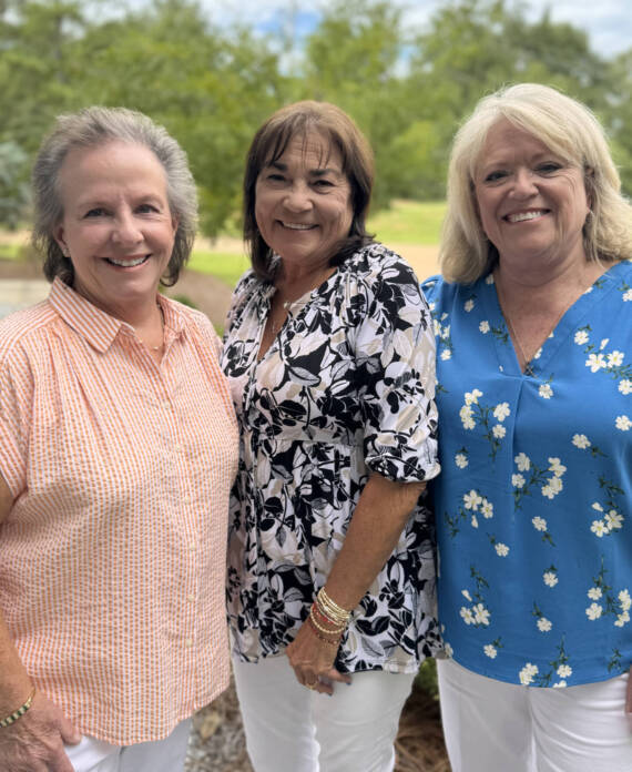 Three smiling women wearing floral tops.