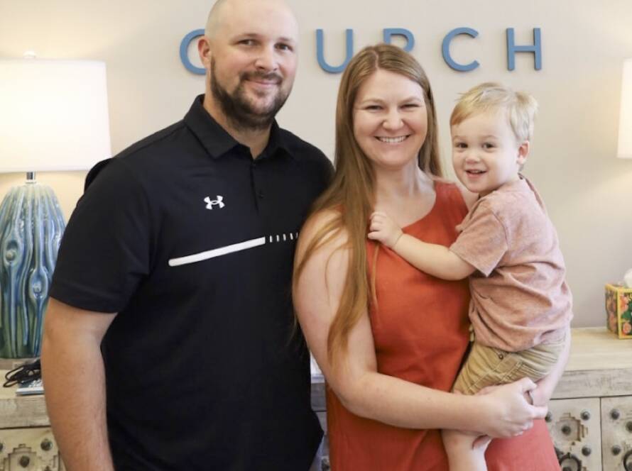 Family smiling in front of church sign.