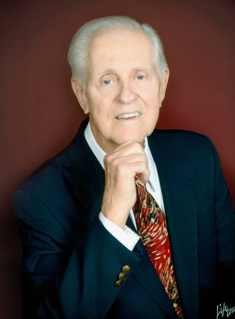 Elderly man in suit with red tie.