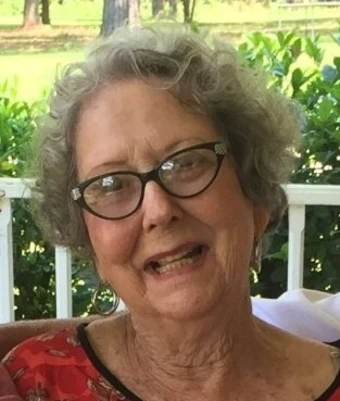 Elderly woman smiling with glasses outside.