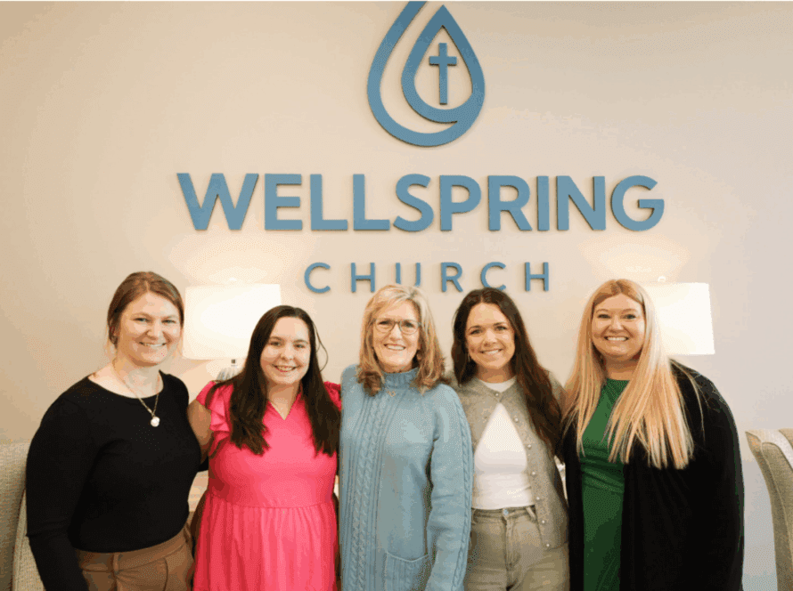 Five women smiling in front of church sign.
