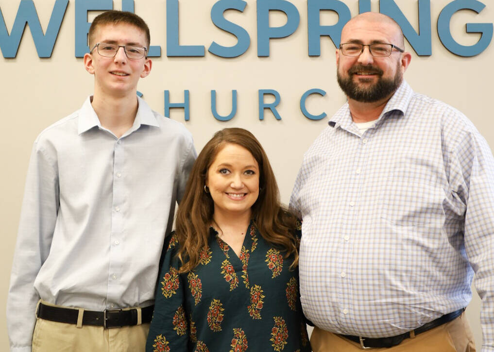 Three smiling adults in front of Wellspring sign