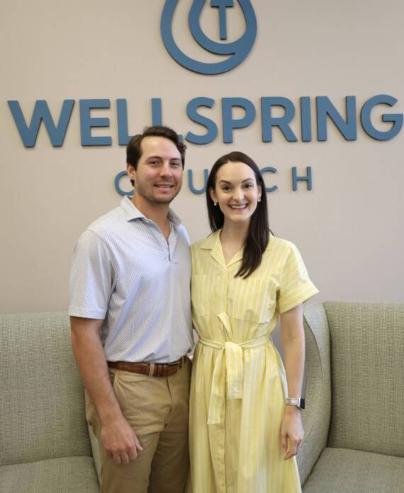 Smiling man and woman by Wellspring Church sign