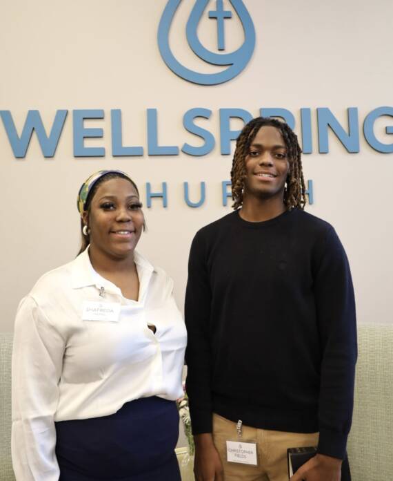 Two people smiling in front of Wellspring sign